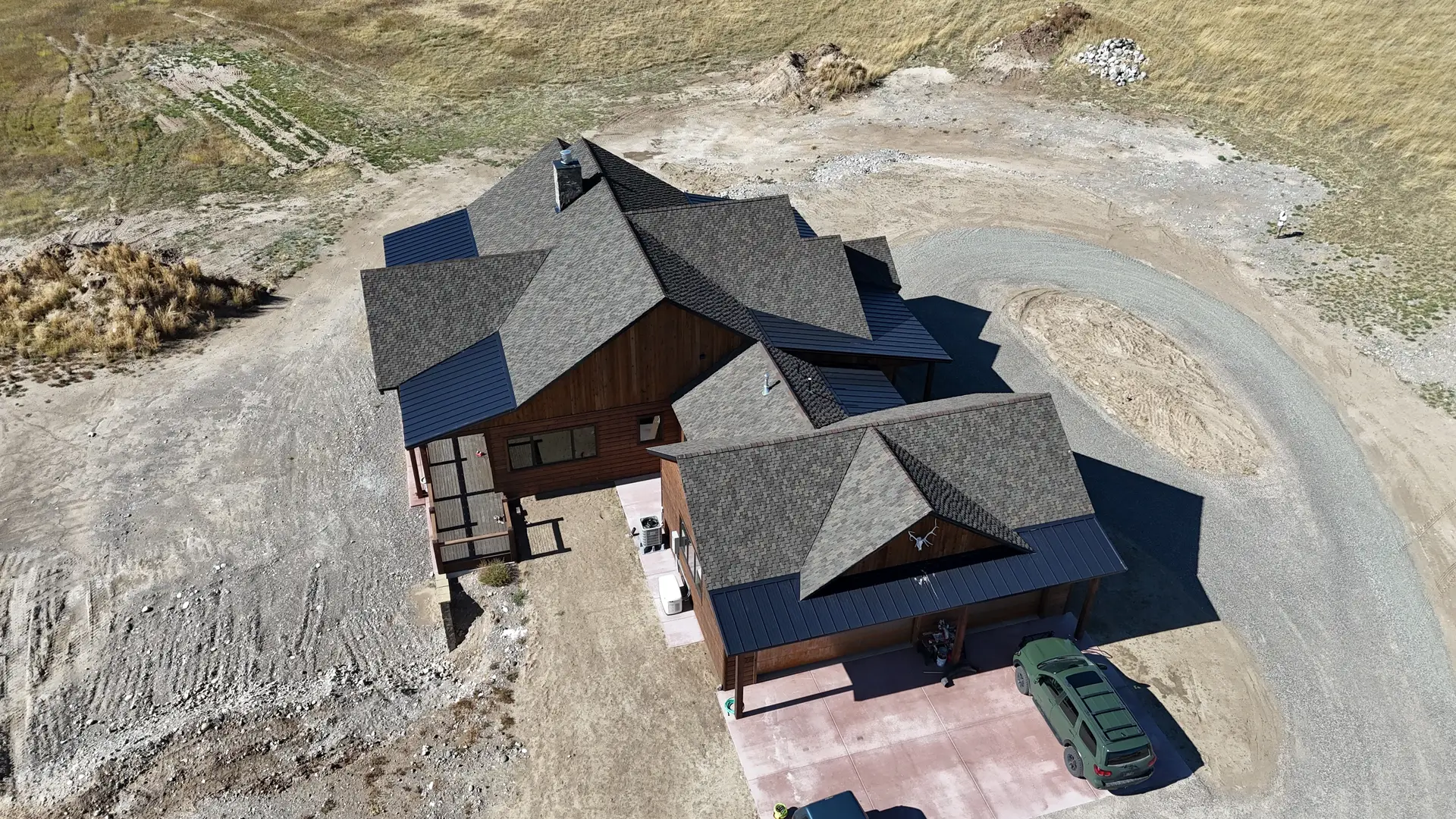 A drone view of a new home with a dark shingled roof and a fresh gravel drive
