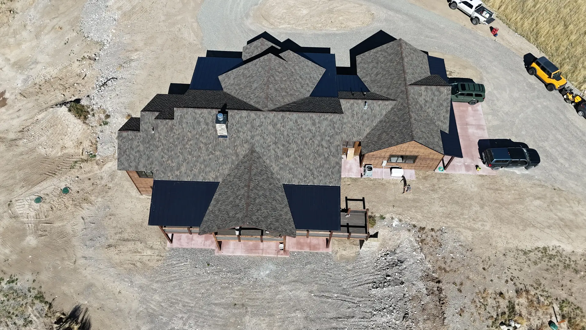 A drone view down onto the complex shingled roofline of a large finished home