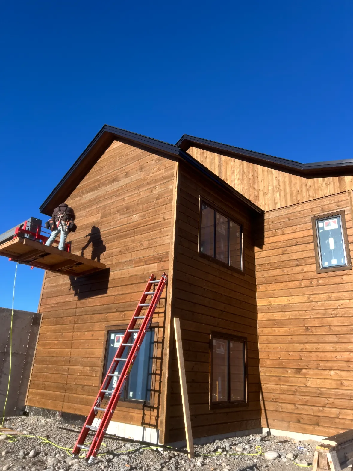 A two-storey home in stained wood siding, a ladder still leaning against the wall