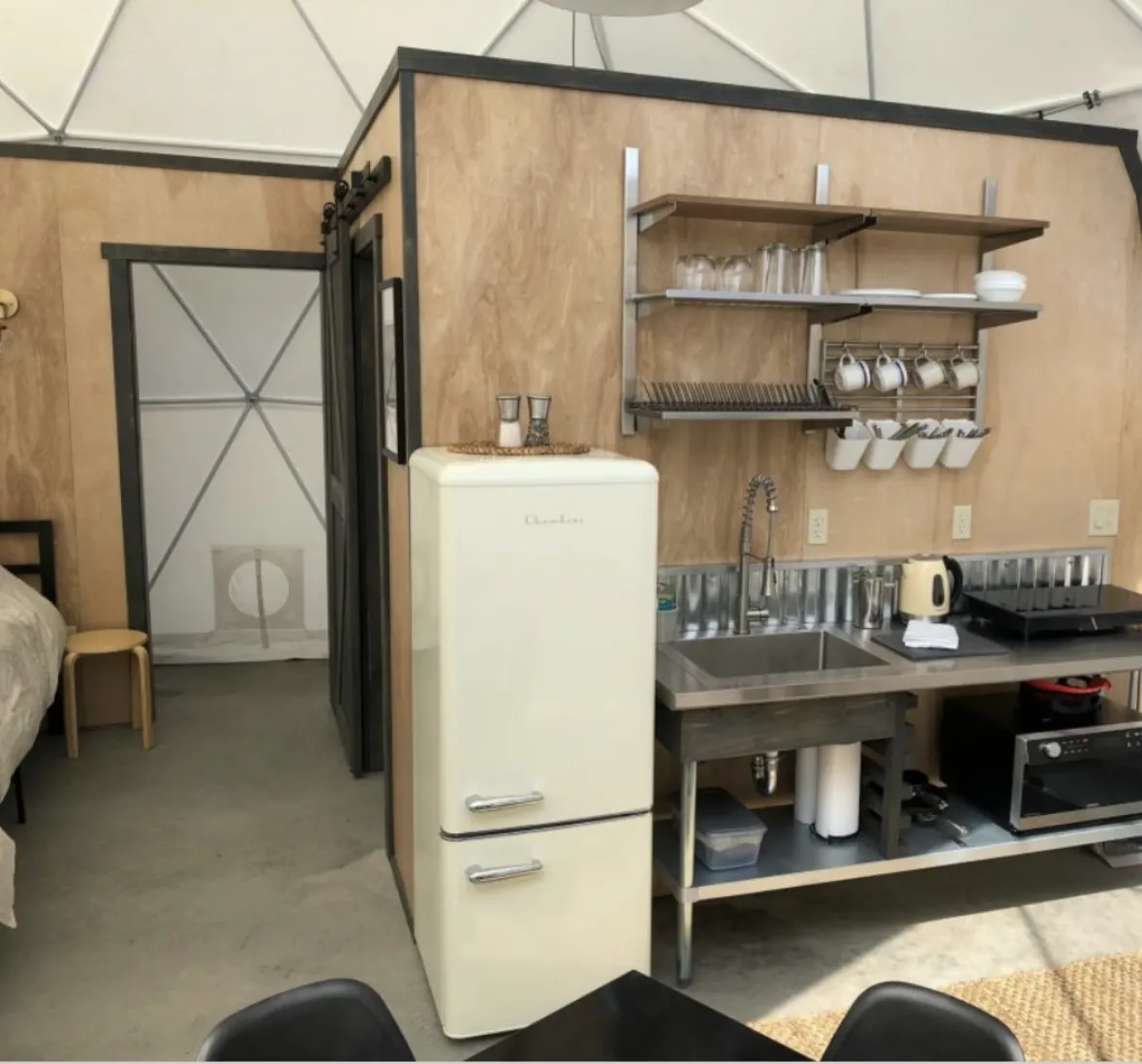 A kitchenette inside a dome: open steel shelving, a stainless sink and a cream retro fridge