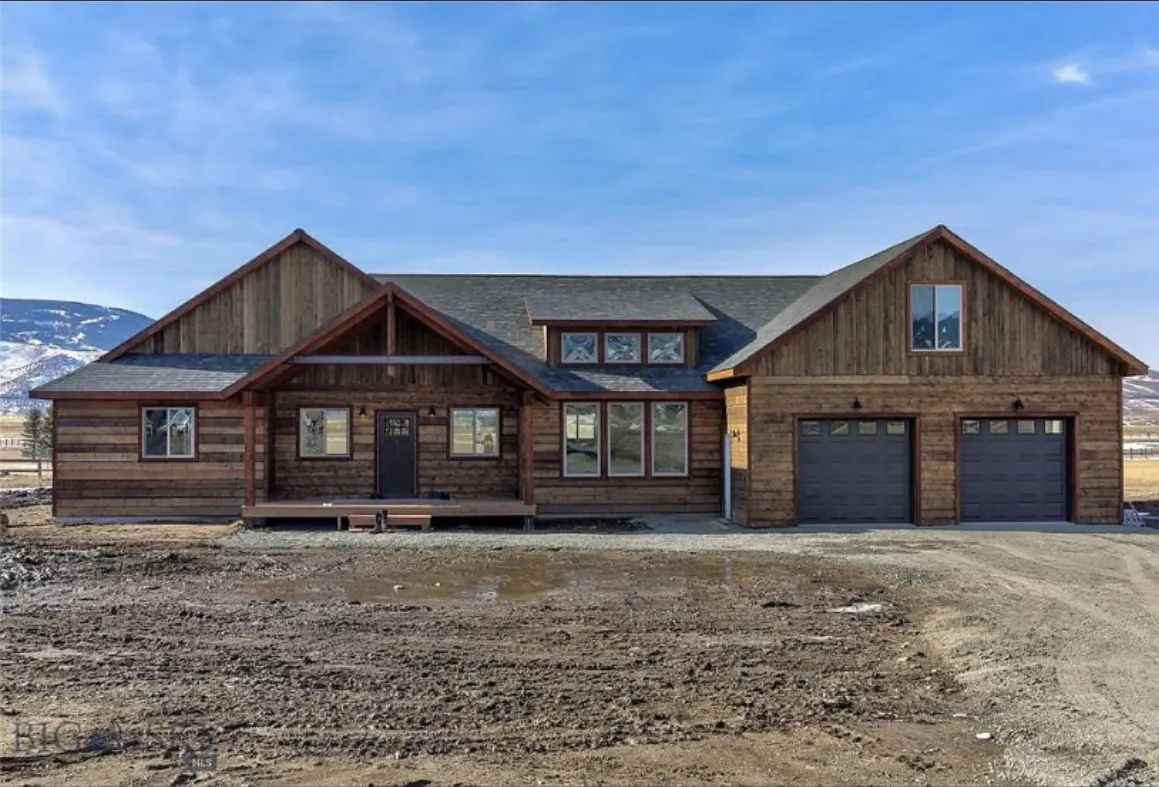 A timber-sided ranch home with a covered entry and two garage bays