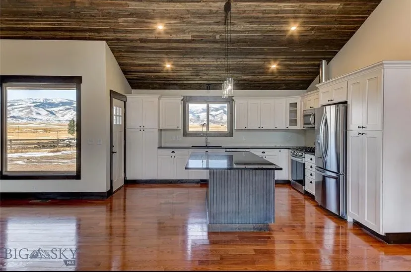 A kitchen with white shaker cabinets, a wood-plank ceiling and a picture window onto snowy hills