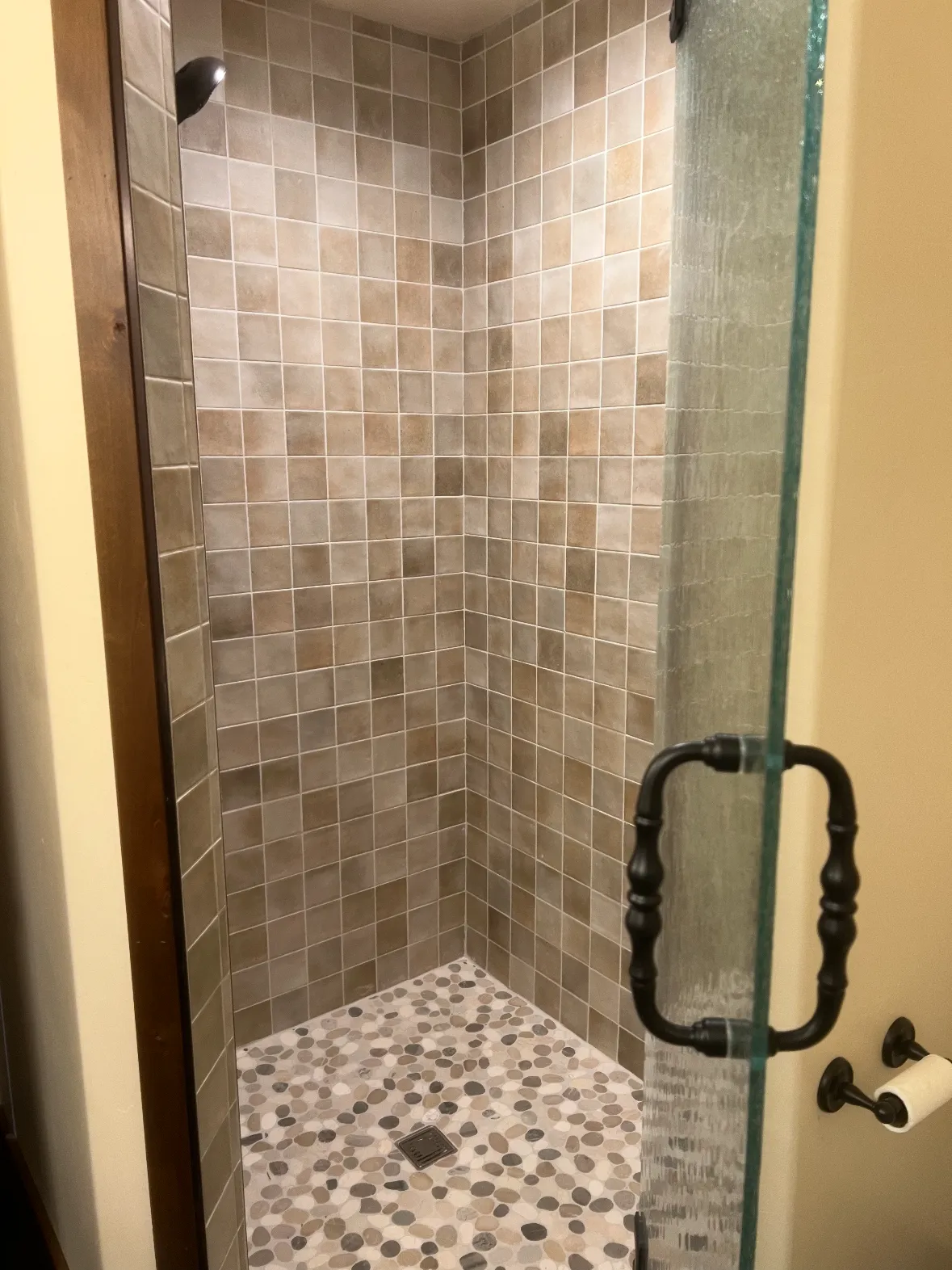 A walk-in shower in earth-toned tile with a river-pebble floor behind a glass door