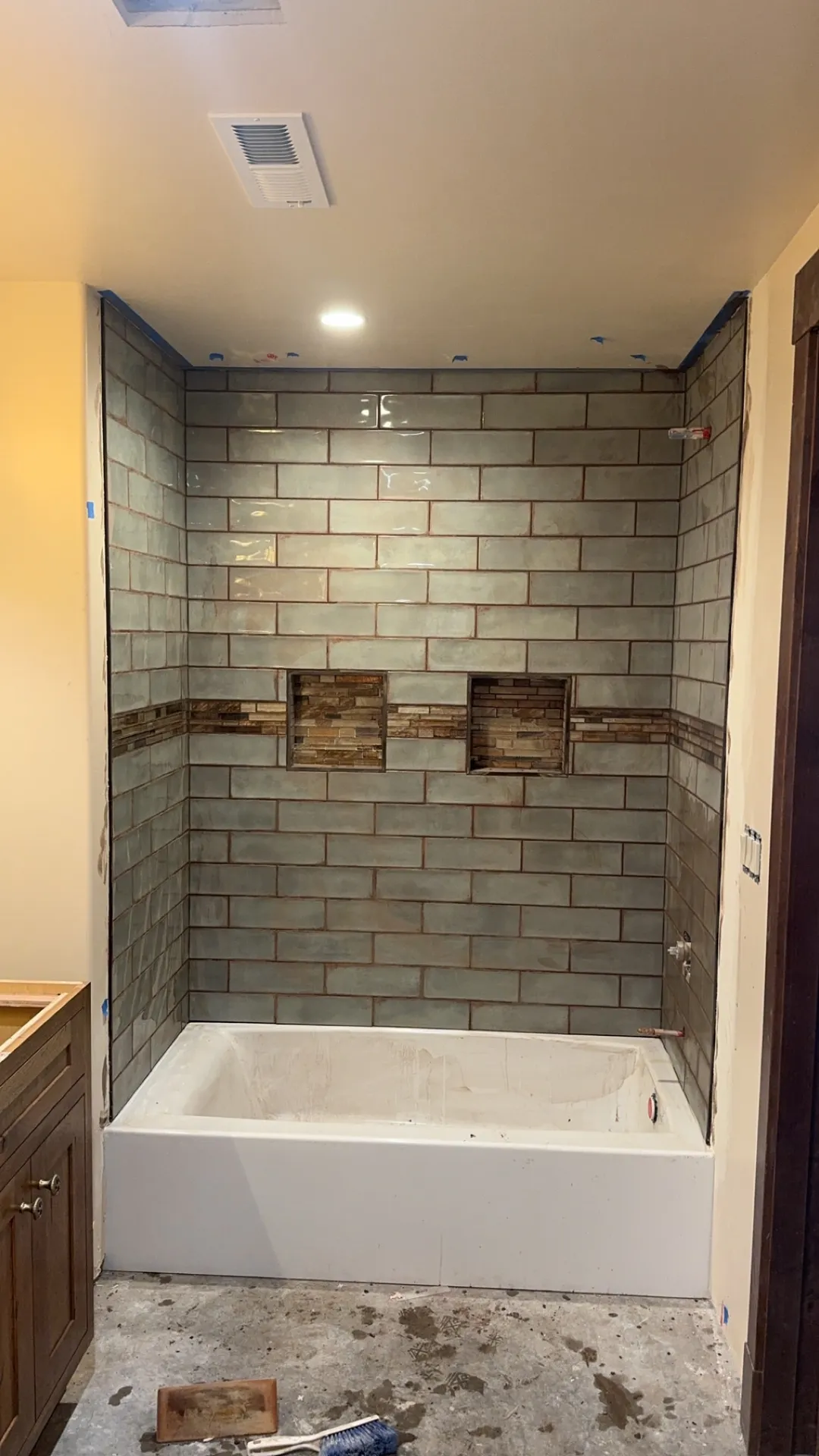 A tub surround in grey stone-look tile with a band of accent tile and two recessed niches